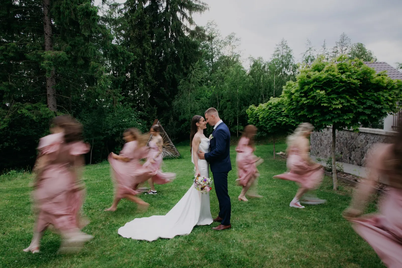 Novomanželia sa bozkávajú, okolo nich tancujú družičky